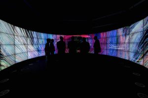 Silhouetted people in front of multiple screens