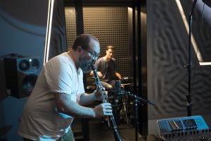 One man playing saxophone, another playing electronic drums