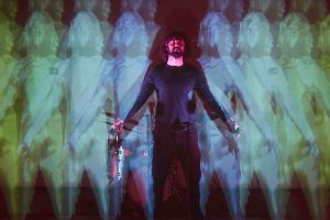 A man stands in front of a screen with a projection showing the outlines of bodies on it