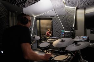 Two people playing electronic drum kits in a sound studio