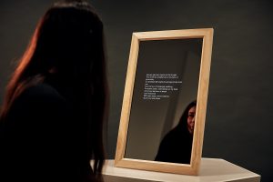 A woman looking at a mirror that is displaying poetry