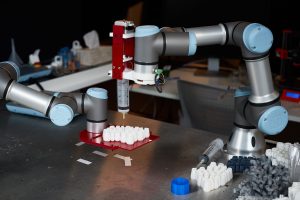 A robot arm with a syringe attached is inserted liquid into a 3D printed object
